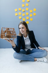 Young businesswoman holding architectural model with yellow sticky notes on the wall behind ger - GUSF01720