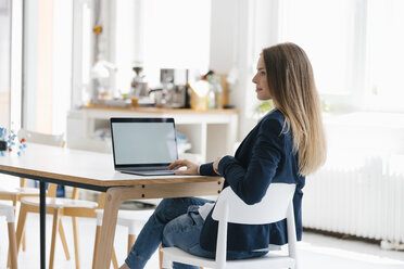 Junge Geschäftsfrau sitzt im Büro und benutzt einen Laptop - GUSF01735