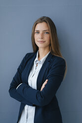 Portrait of a young businesswoman against blue background, with arms crossed - GUSF01740