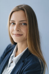 Porträt einer jungen Geschäftsfrau vor blauem Hintergrund, die selbstbewusst lächelt - GUSF01741