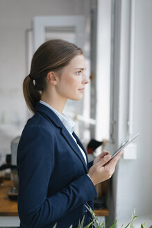 Junge Geschäftsfrau, die am Fenster steht und ein digitales Tablet benutzt - GUSF01742