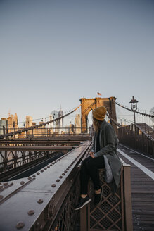 USA, New York, New York City, weibliche Touristin sitzt auf der Brooklyn Bridge im Morgenlicht - LHPF00318