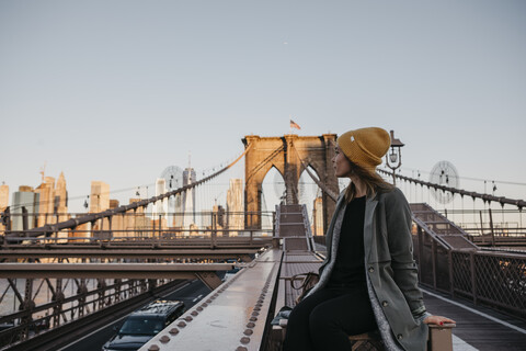 USA, New York, New York City, weibliche Touristin sitzt auf der Brooklyn Bridge im Morgenlicht, lizenzfreies Stockfoto