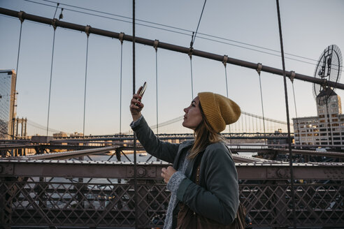 USA, New York, New York City, weibliche Touristin mit Smartphone auf der Brooklyn Bridge im Morgenlicht - LHPF00321