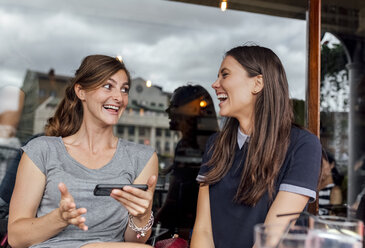 Zwei Frauen haben Spaß mit ihrem Smartphone auf einer Terrasse - MGOF03884