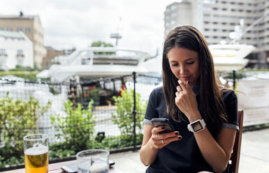 Junge schöne Frau benutzt ihr Smartphone auf einer Terrasse - MGOF03886
