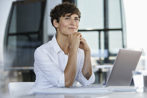 Lächelnde Geschäftsfrau sitzt am Schreibtisch im Büro mit Laptop - RBF06853
