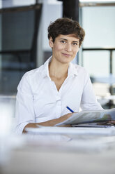 Porträt einer selbstbewussten Geschäftsfrau, die mit einem Laptop und einem Dokument am Schreibtisch sitzt - RBF06856