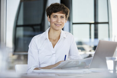 Portrait of confident businesswoman sitting at desk in office with laptop and document - RBF06857