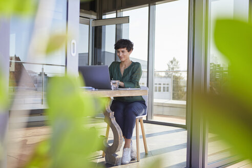 Smiling businesswoman sitting at table using laptop - RBF06863