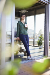 Smiling businesswoman leaning against table having a coffee break - RBF06866