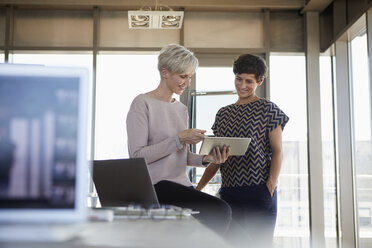 Two smiling businesswomen sharing tablet in office - RBF06867