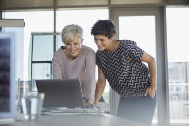 Two smiling businesswomen sharing laptop at desk in office - RBF06871