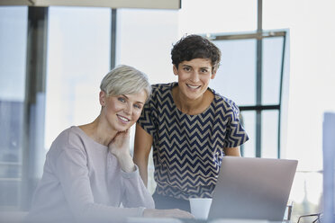 Porträt von zwei lächelnden Geschäftsfrauen mit Laptop am Schreibtisch im Büro - RBF06873