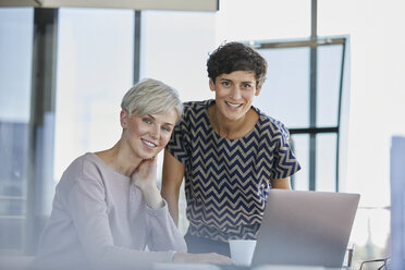 Portrait of two smiling businesswomen with laptop at desk in office - RBF06873