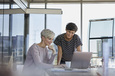 Zwei lächelnde Geschäftsfrauen teilen sich einen Laptop am Schreibtisch im Büro - RBF06874