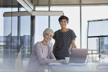 Portrait of two smiling businesswomen with laptop at desk in office - RBF06875