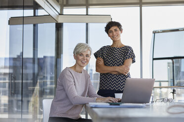 Portrait of two smiling businesswomen with laptop at desk in office - RBF06876