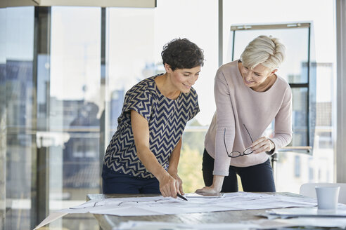 Zwei lächelnde Geschäftsfrauen besprechen einen Plan auf dem Schreibtisch im Büro - RBF06881
