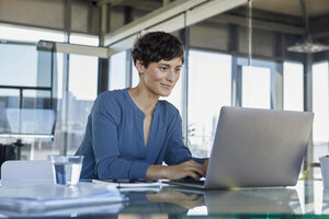 Geschäftsfrau sitzt am Schreibtisch im Büro und benutzt einen Laptop - RBF06884