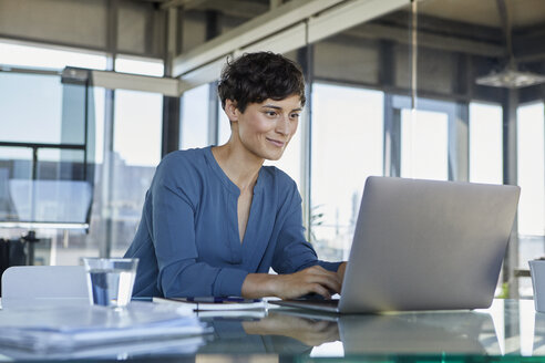 Businesswoman sitting at desk in office using laptop - RBF06884