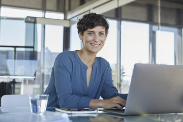 Portrait of confident businesswoman sitting at desk in office with laptop - RBF06885