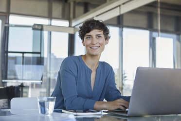 Smiling businesswoman sitting at desk in office with laptop - RBF06886