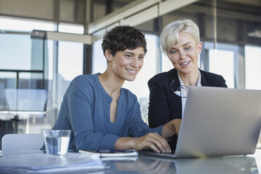 Two smiling businesswomen sharing laptop at desk in office - RBF06887
