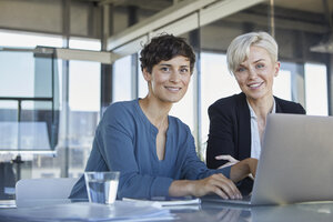 Porträt von zwei lächelnden Geschäftsfrauen mit Laptop am Schreibtisch im Büro - RBF06888