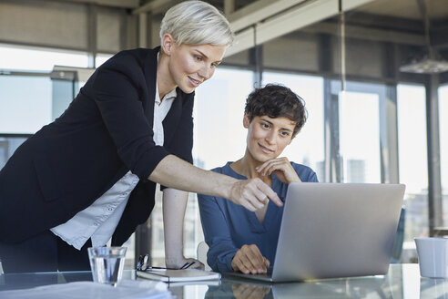 Zwei lächelnde Geschäftsfrauen teilen sich einen Laptop am Schreibtisch im Büro - RBF06889