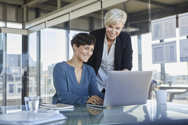 Two smiling businesswomen sharing laptop at desk in office - RBF06890