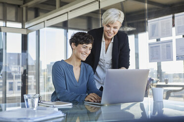 Zwei lächelnde Geschäftsfrauen teilen sich einen Laptop am Schreibtisch im Büro - RBF06890