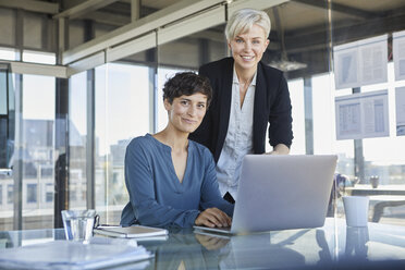 Porträt von zwei lächelnden Geschäftsfrauen mit Laptop am Schreibtisch im Büro - RBF06891