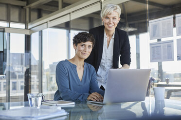 Portrait of two smiling businesswomen with laptop at desk in office - RBF06891