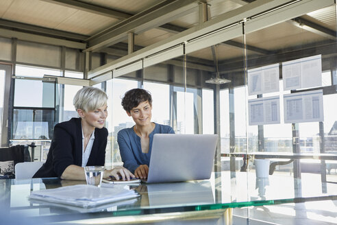 Two smiling businesswomen sharing laptop at desk in office - RBF06893