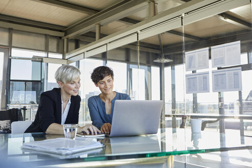 Zwei lächelnde Geschäftsfrauen teilen sich einen Laptop am Schreibtisch im Büro - RBF06893