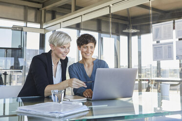 Two smiling businesswomen sharing laptop at desk in office - RBF06894