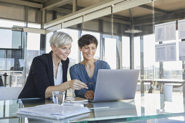 Zwei lächelnde Geschäftsfrauen teilen sich einen Laptop am Schreibtisch im Büro - RBF06894