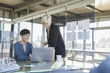 Zwei lächelnde Geschäftsfrauen teilen sich einen Laptop am Schreibtisch im Büro - RBF06897