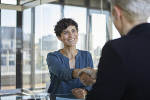 Zwei Geschäftsfrauen beim Händeschütteln am Schreibtisch im Büro - RBF06900