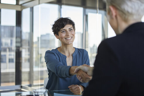 Two businesswomen shaking hands at desk in office - RBF06900