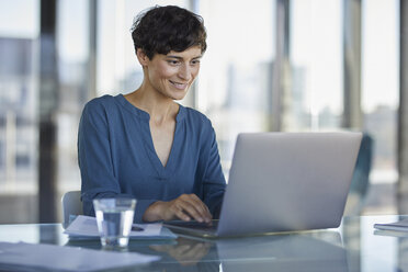 Geschäftsfrau sitzt am Schreibtisch im Büro und benutzt einen Laptop - RBF06903