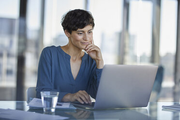 Businesswoman sitting at desk in office using laptop - RBF06904