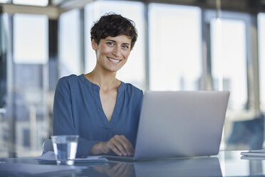 Portrait of confident businesswoman sitting at desk in office with laptop - RBF06906