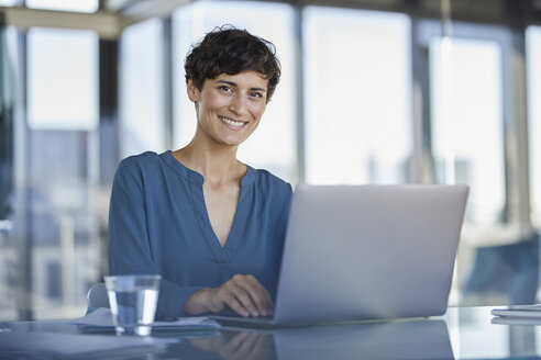 Porträt einer selbstbewussten Geschäftsfrau, die mit einem Laptop am Schreibtisch sitzt - RBF06906