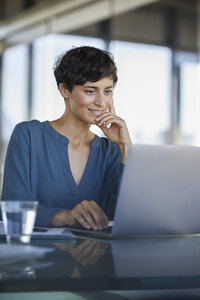 Geschäftsfrau sitzt am Schreibtisch im Büro und benutzt einen Laptop - RBF06907