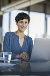 Portrait of confident businesswoman sitting at desk in office with laptop - RBF06908