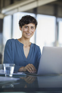 Porträt einer selbstbewussten Geschäftsfrau, die mit einem Laptop am Schreibtisch sitzt - RBF06908