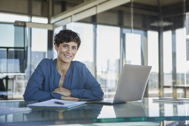 Portrait of confident businesswoman sitting at desk in office with laptop - RBF06914
