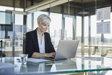 Geschäftsfrau sitzt am Schreibtisch im Büro und benutzt einen Laptop - RBF06915